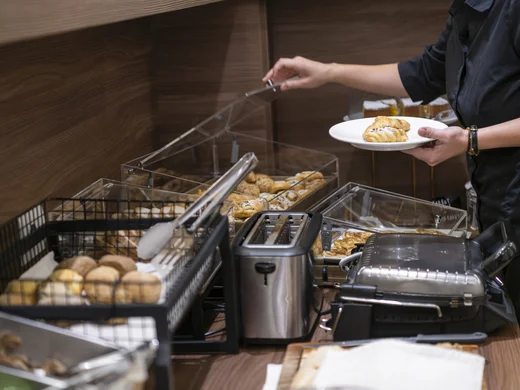 Persona che prende un cornetto da un buffet con tostapane e piastra