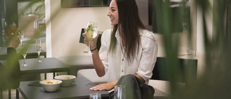 Donna che sorseggia una bevanda in un bar con tavoli e snack