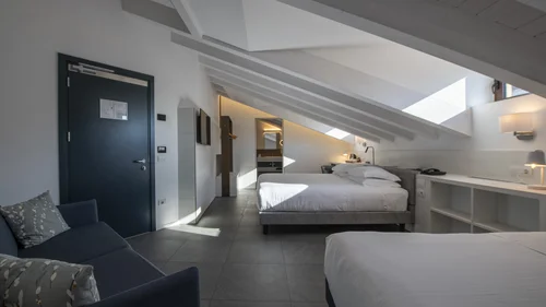 Hotel Touring in Verona | Picture gallery Camera d'hotel mansardata con due letti, divano e luce naturale dalle finestre sul tetto