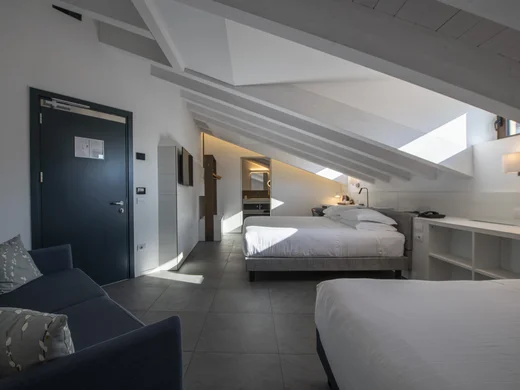 Camera d'hotel mansardata con due letti, divano e luce naturale dalle finestre sul tetto