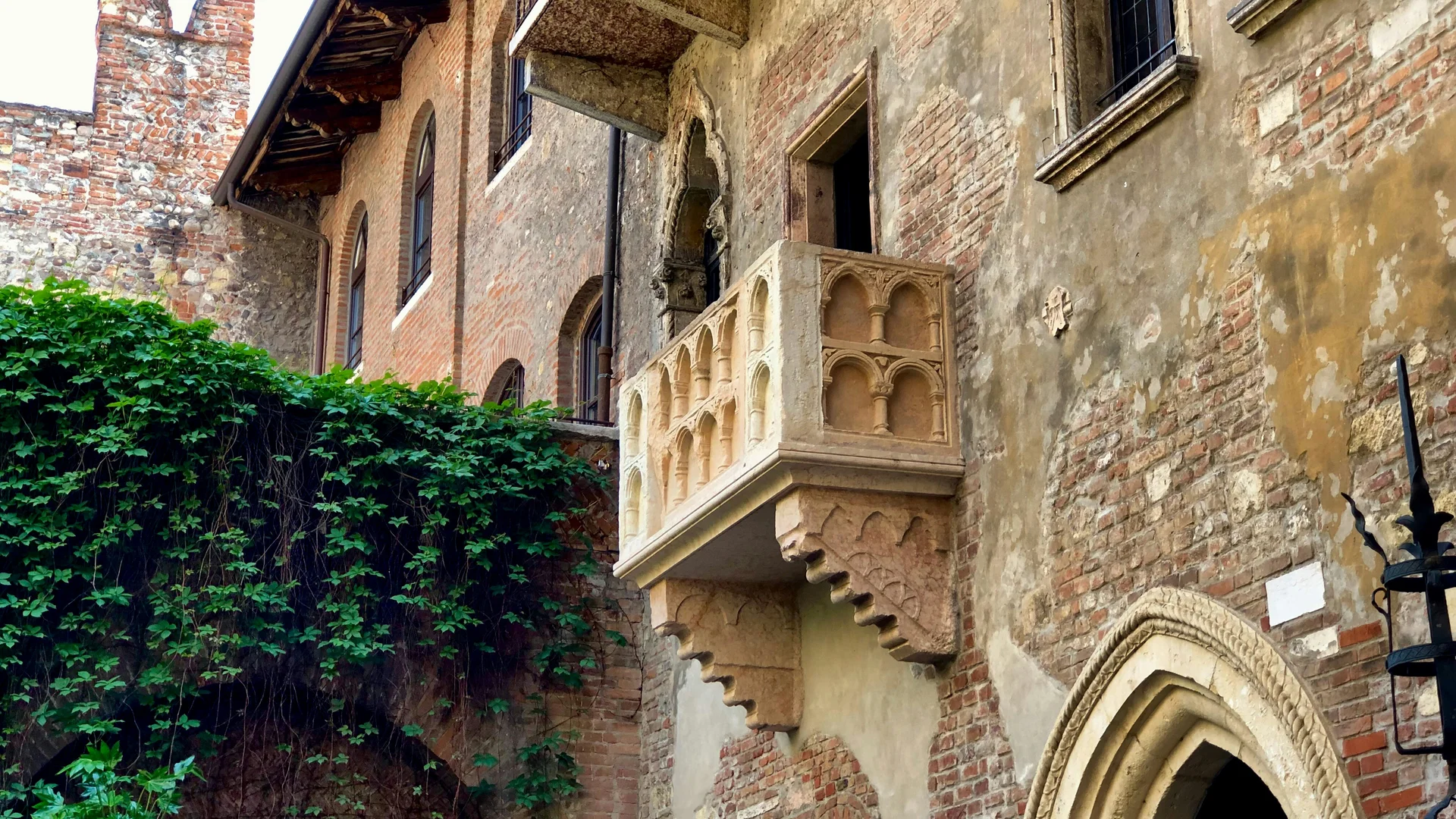 Hotel Touring in Verona | Picture gallery Historic stone balcony on old brick building with green plants growing nearby