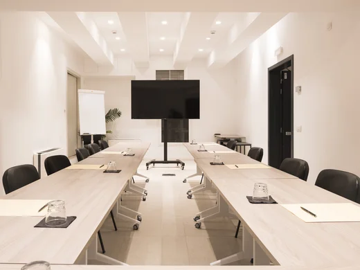 Sala riunioni moderna con tavoli, sedie nere e schermo TV grande
