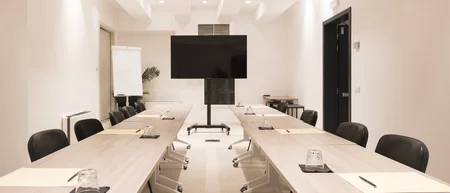 Sala riunioni moderna con tavoli, sedie nere e schermo TV grande