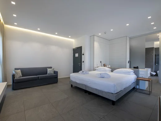 Camera d'albergo moderna con letto matrimoniale e divano grigio