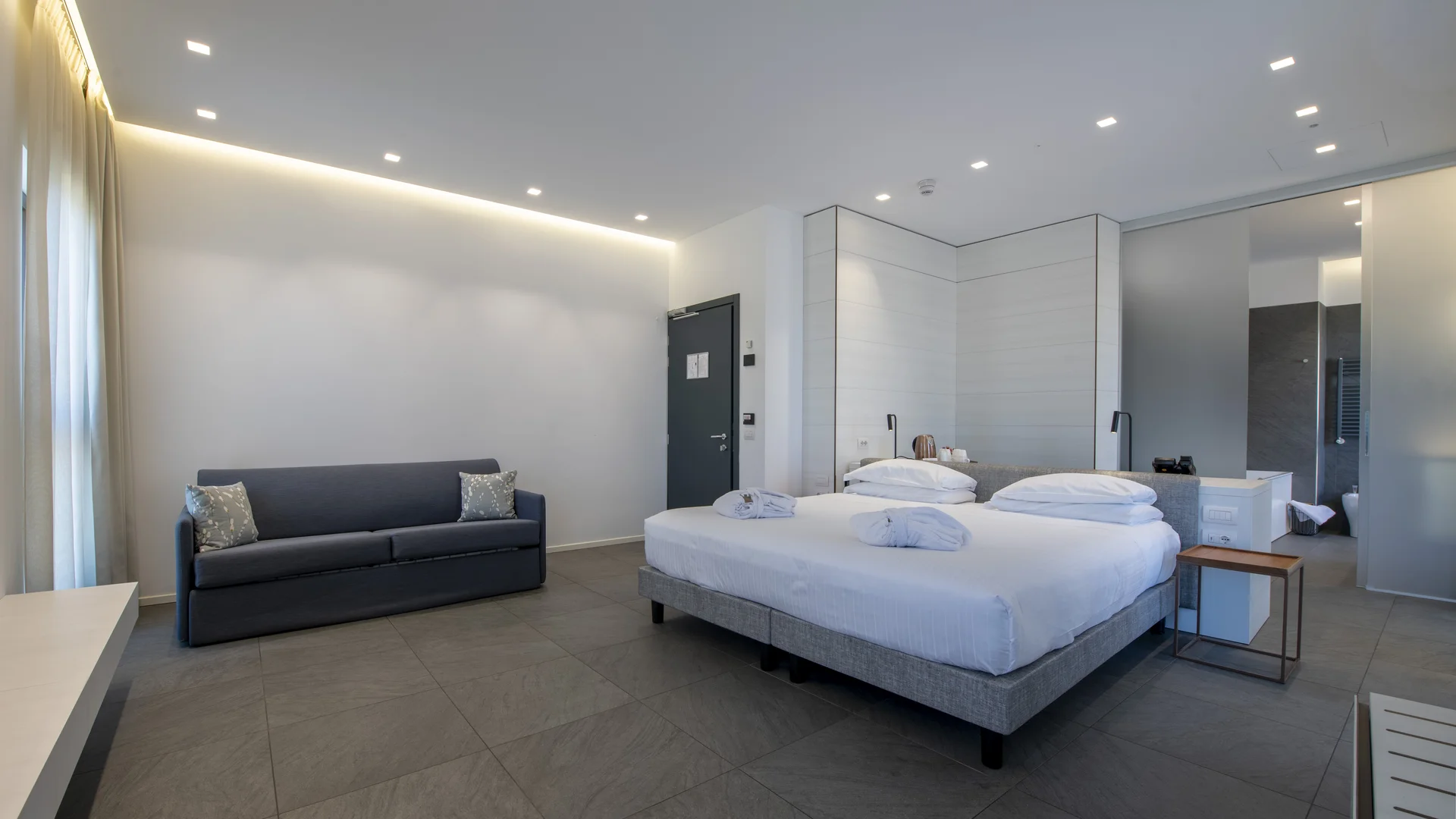 Hotel Touring in Verona | Picture gallery Camera d'albergo moderna con letto matrimoniale e divano grigio