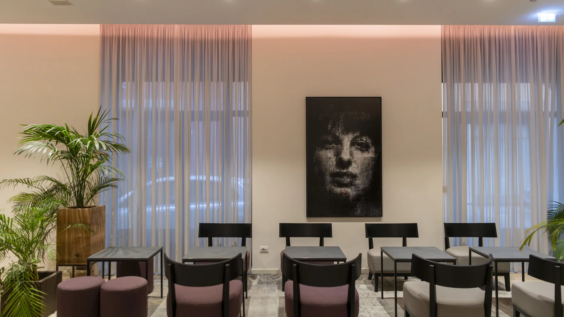 Hotel Touring in Verona | Picture gallery Sala d'attesa moderna con sedie nere, tavoli e quadro di volto femminile