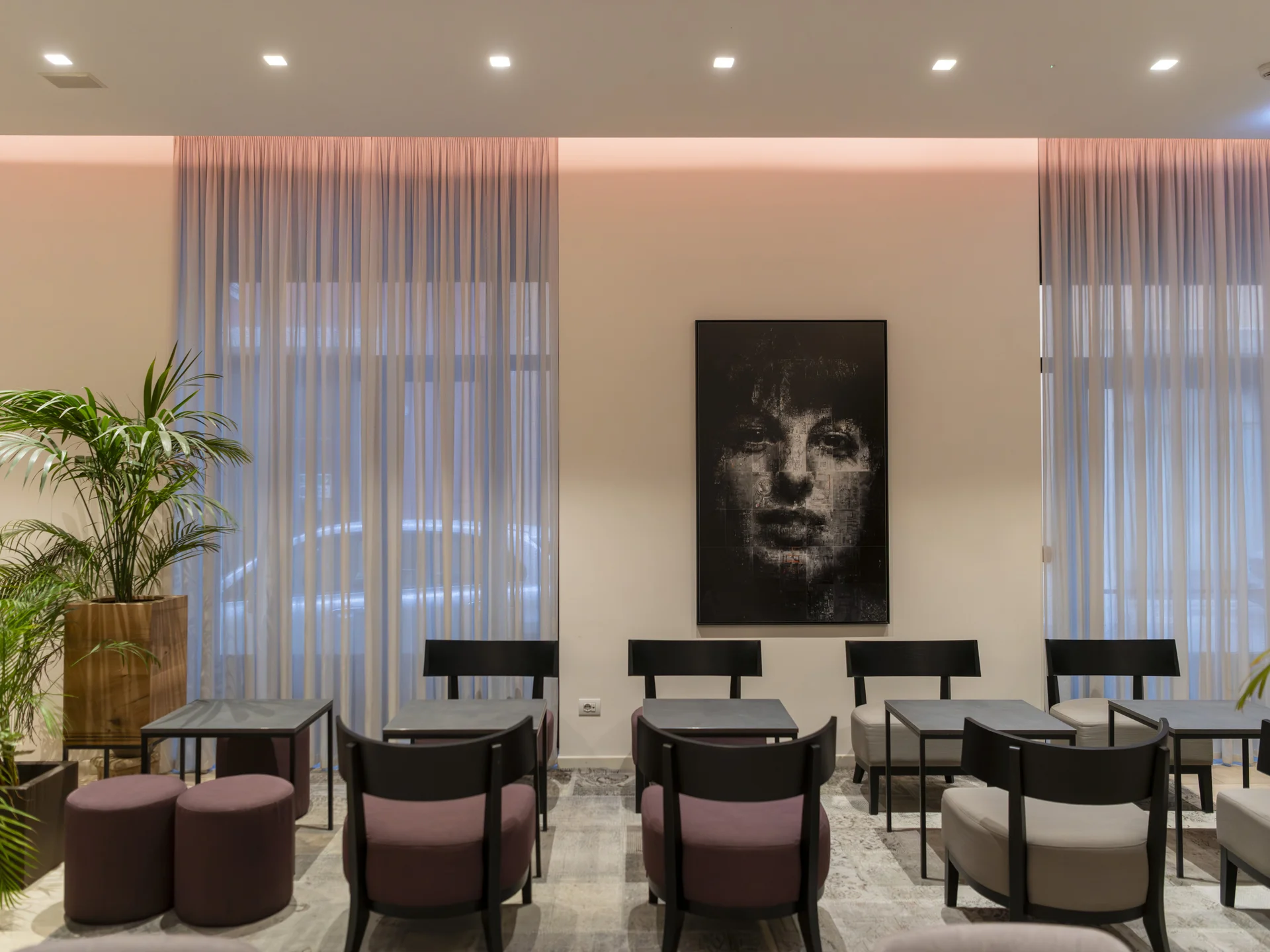 Sala d'attesa moderna con sedie nere, tavoli e quadro di volto femminile