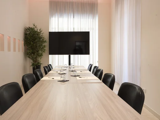Moderner Konferenzraum mit langem Tisch, schwarzen Stühlen und Flachbildschirm