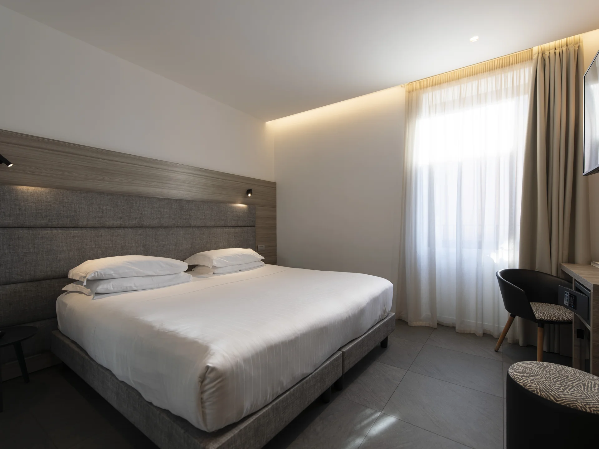 Camera d'albergo moderna con letto matrimoniale, scrivania e finestra con tende