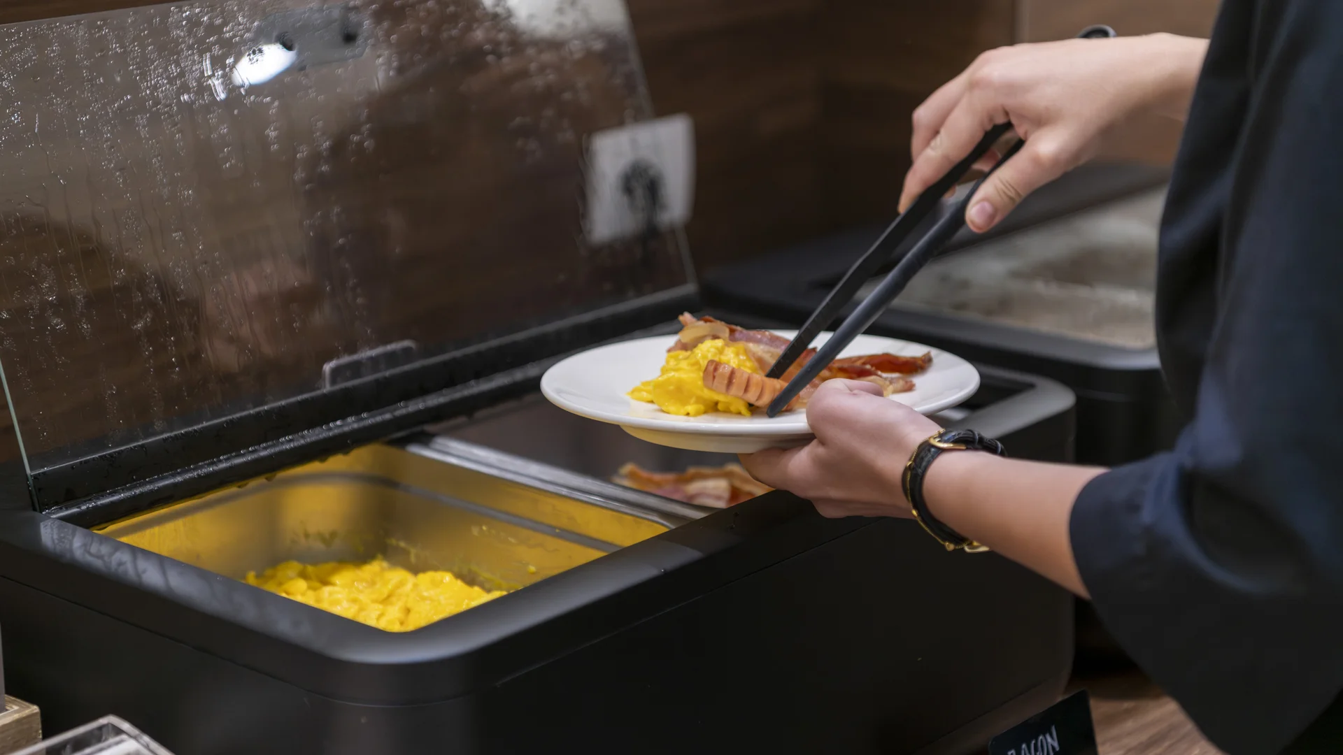 Hotel Touring in Verona | Picture gallery Persona che serve uova strapazzate e bacon da un buffet con pinze
