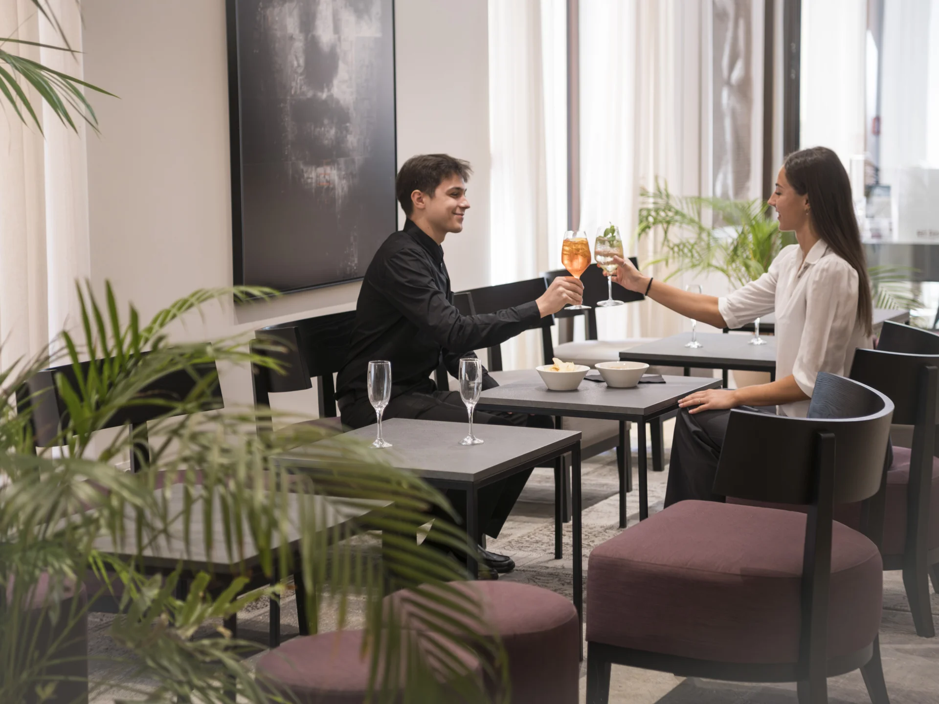 Paar stößt mit Cocktails in einer modernen Bar mit Pflanzen an